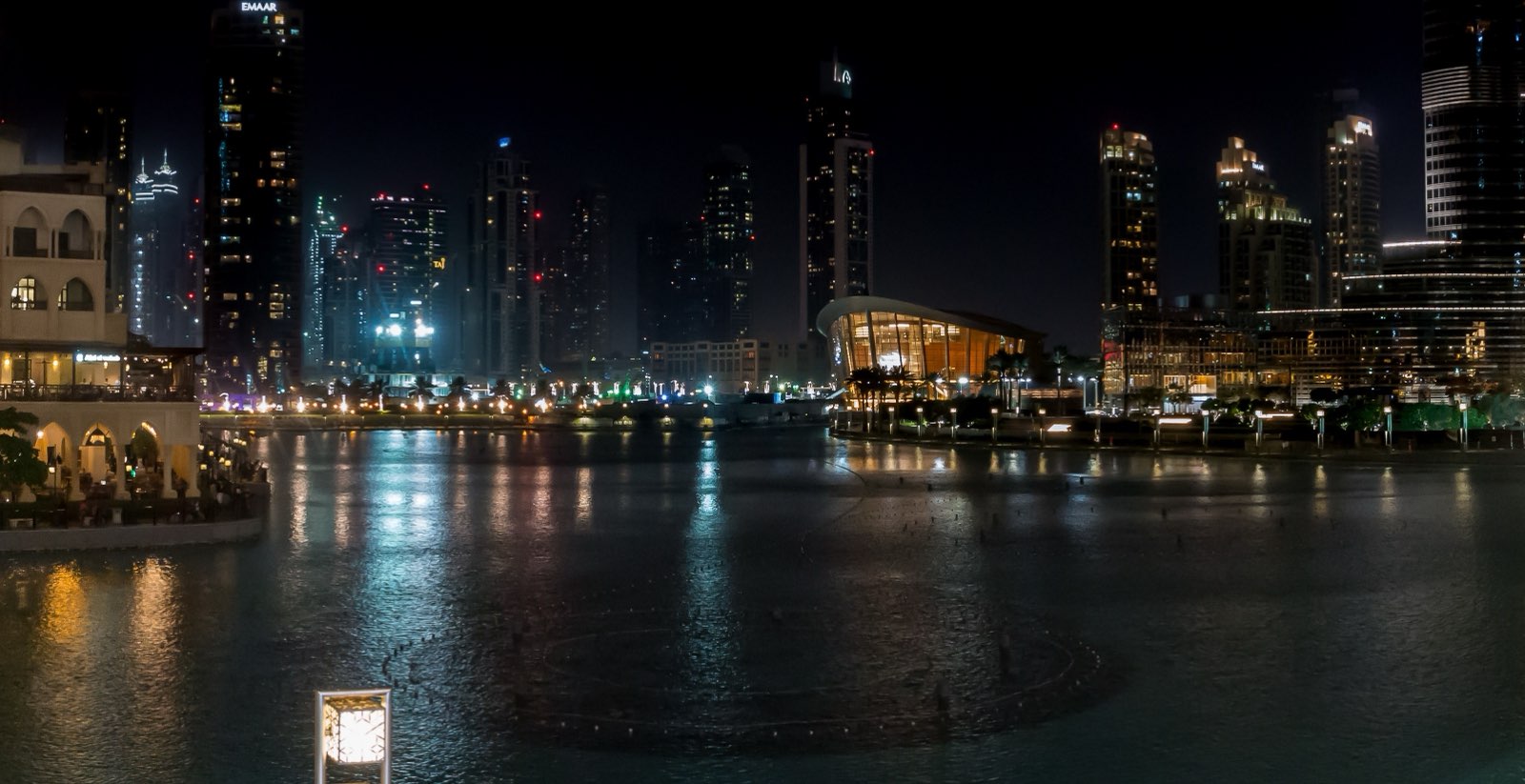 Здание Dubai Opera в форме лодки-доу, подсвеченное ночью, на берегу озера с фонтанами в Даунтауне