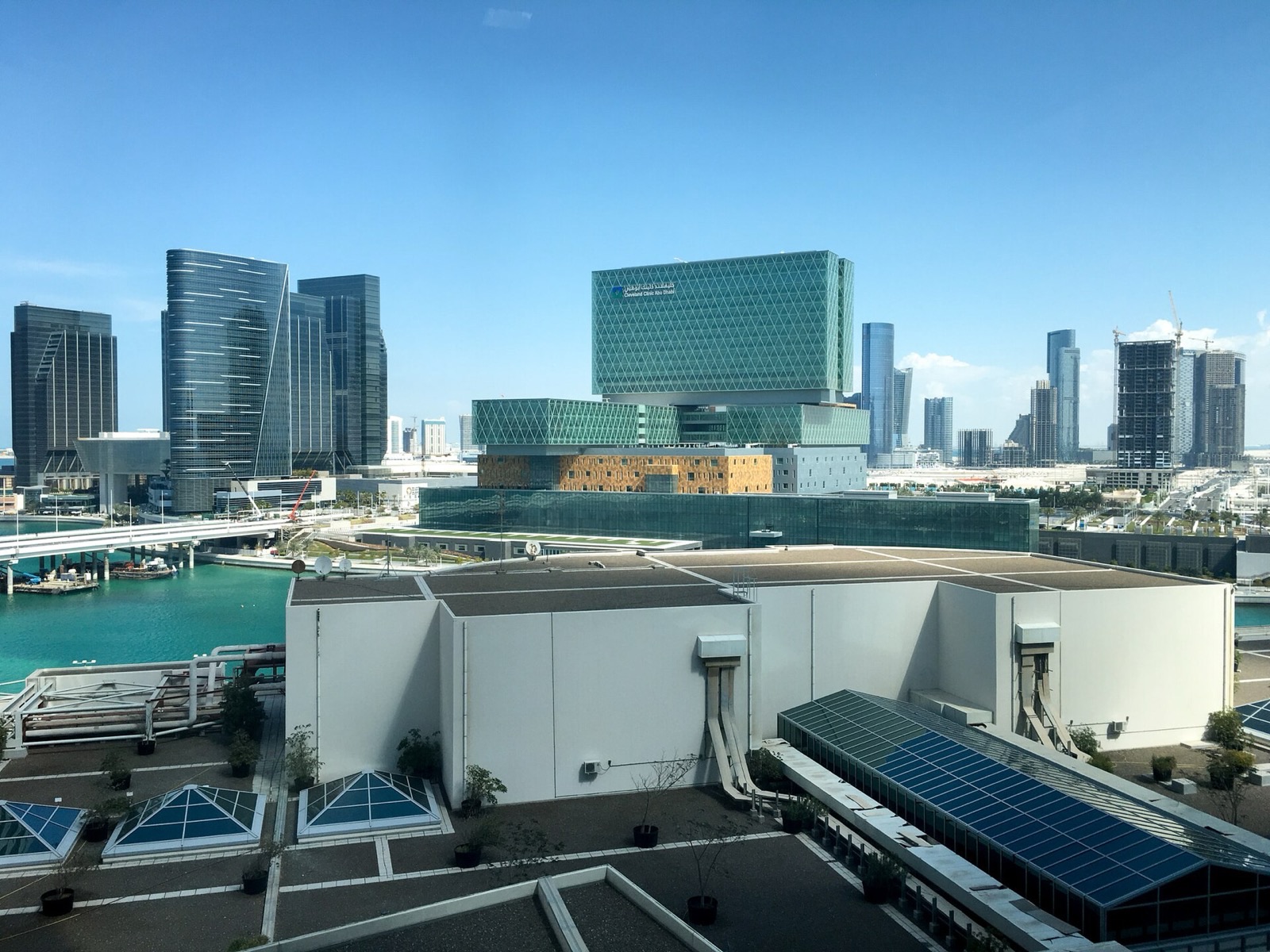 Зелёное стеклянное здание больницы Cleveland Clinic Abu Dhabi на острове Аль-Марьях среди небоскрёбов